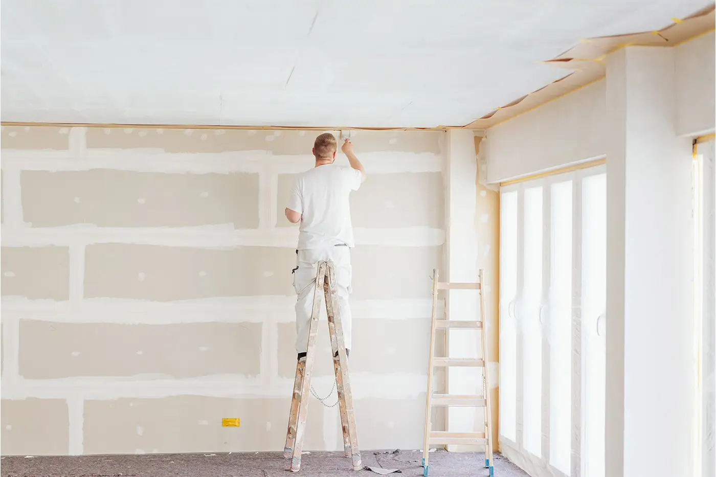 Ein Maler auf der Leister streicht eines Trockenbauwand