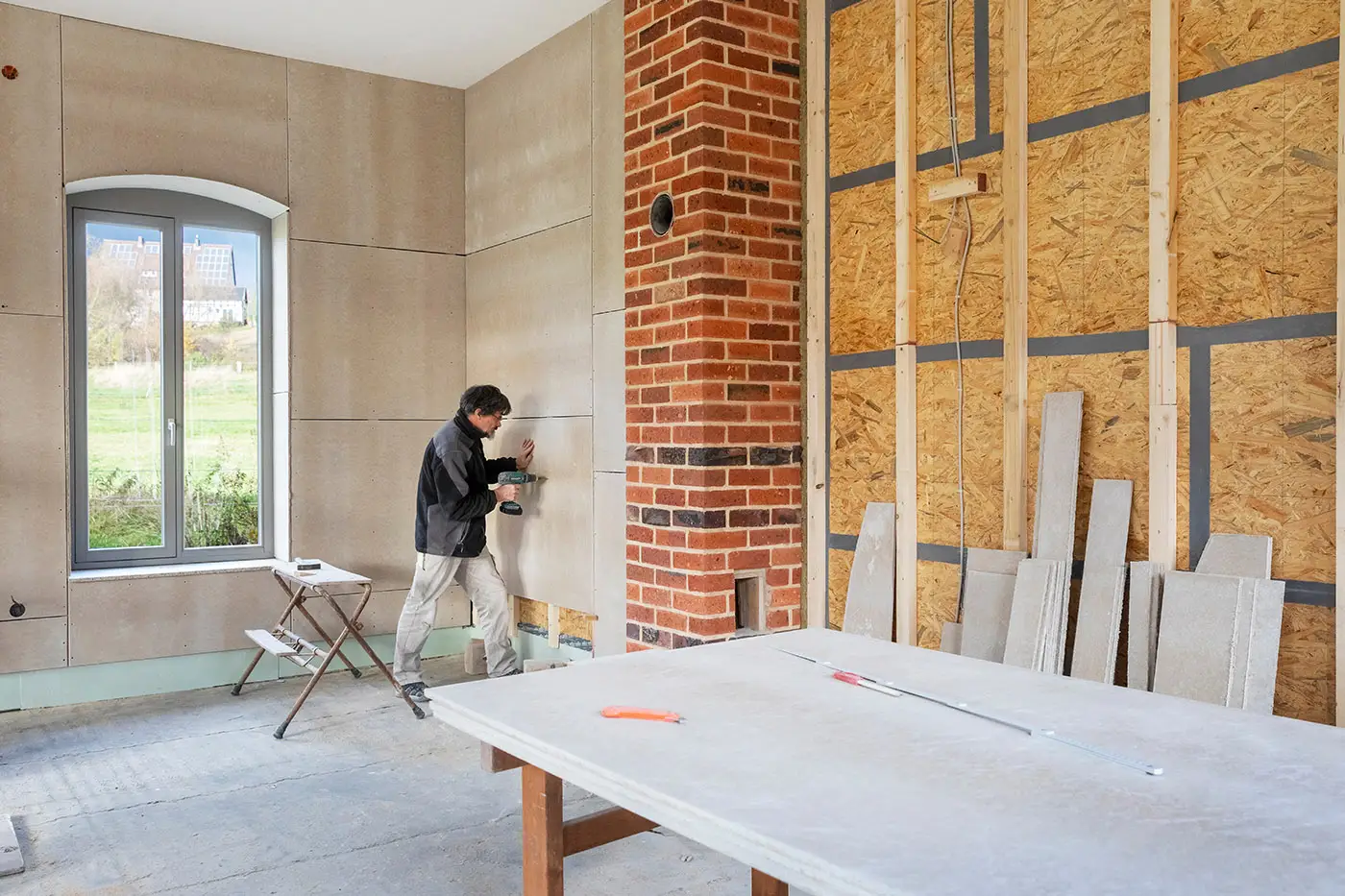 Ein Arbeiter bringt beige Wandfliesen bei Innenausbauarbeiten an einem Wohnzimmer an