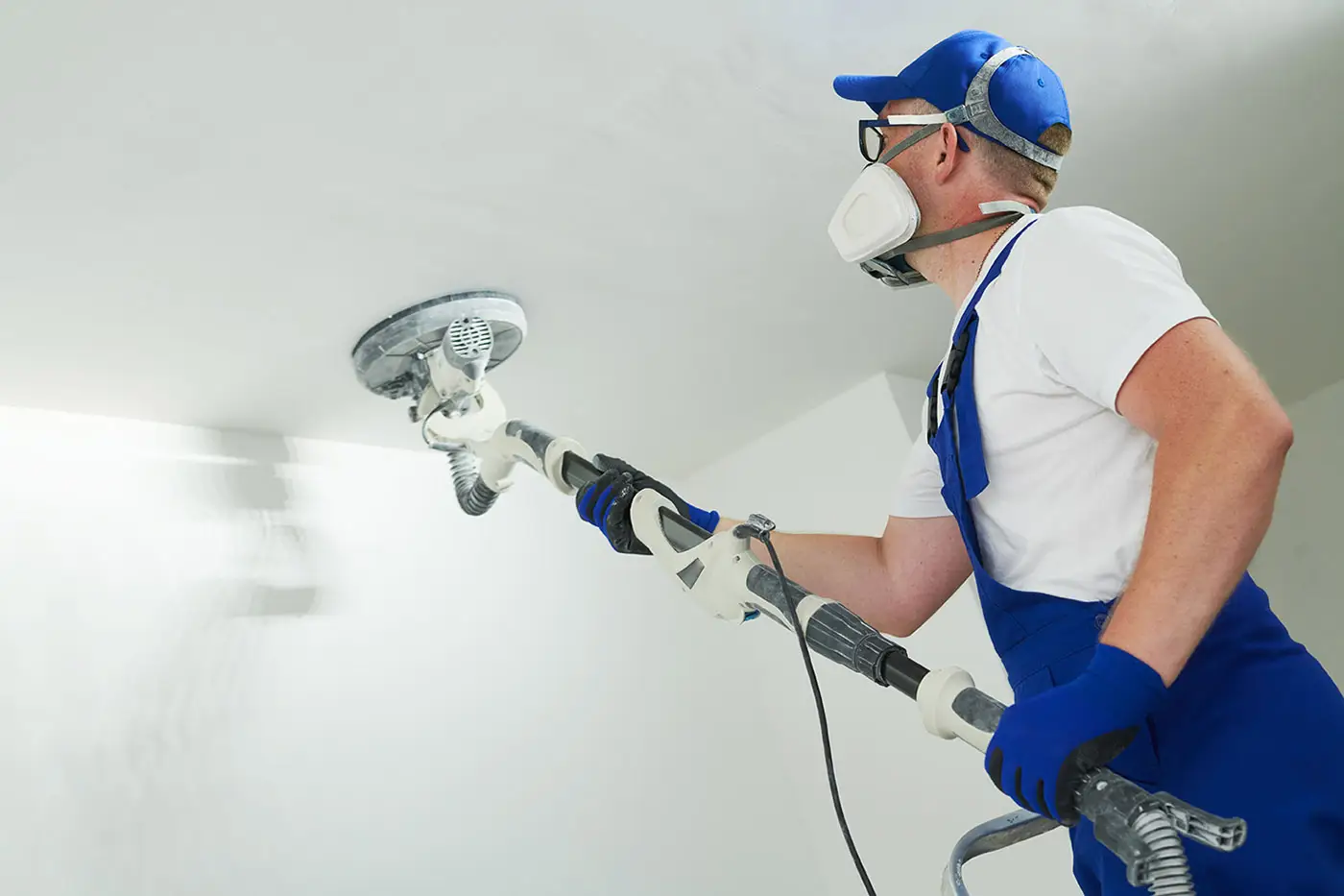 Ein Arbeiter mit Schutzmaske beim Verputzen einer Decke