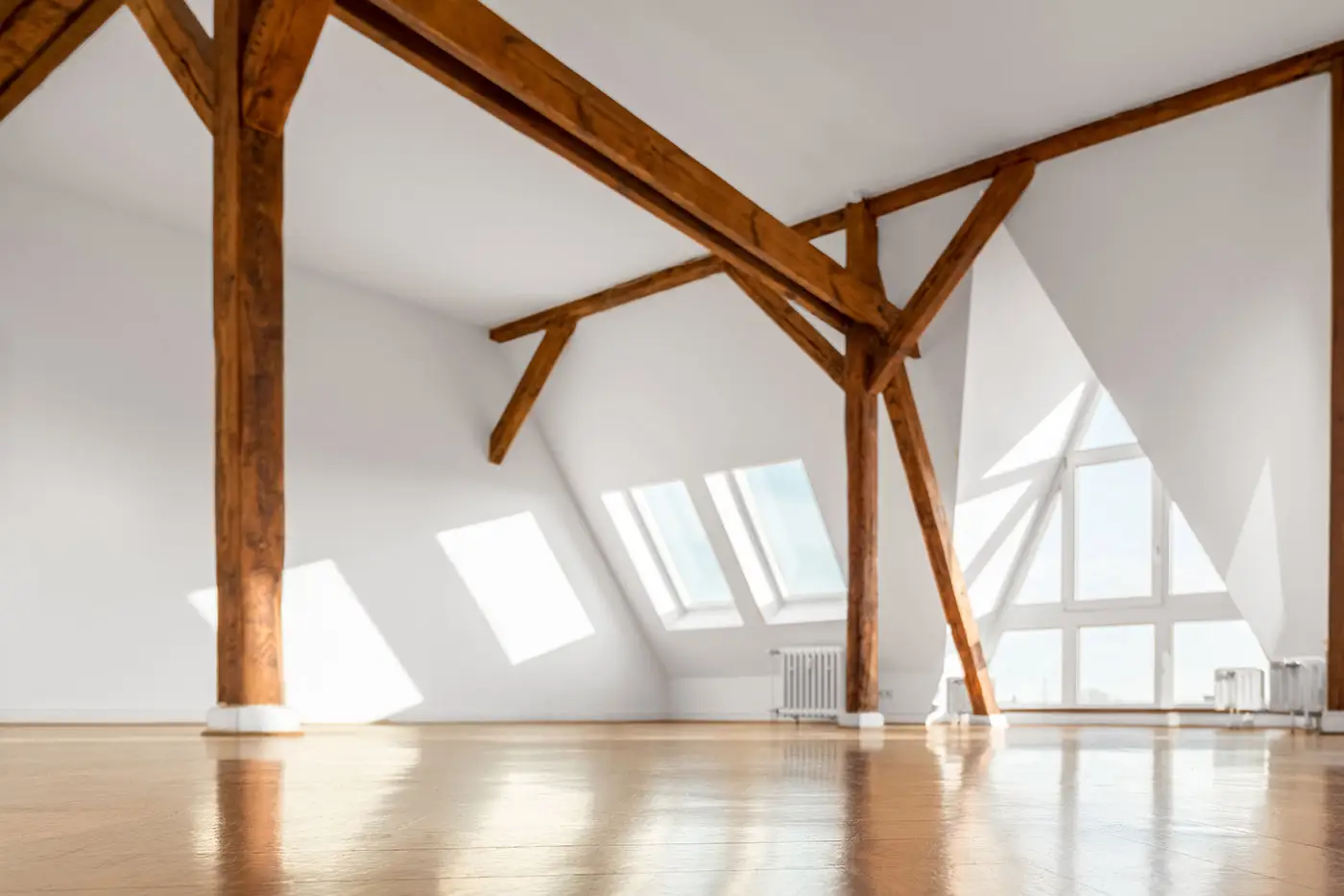 Ein frisch ausgebautes Dachgeschoss mit weißen Dachschrägen und Wänden und hölzernen Trägern